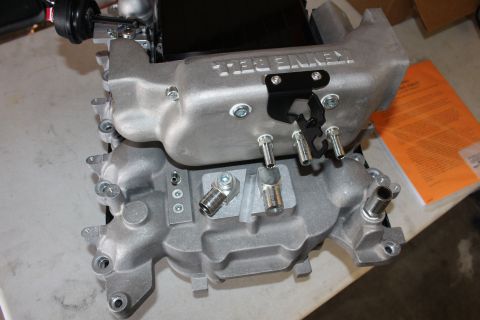 2003 Ford Crown Victoria - aluminum supercharger manifold base with a black Kenne Bell unit, mounting studs and ports photographed at an angle on a bench.