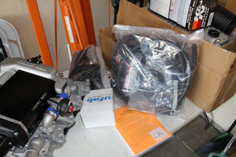 2003 Ford Crown Victoria - Assorted supercharger kit components including bagged hoses, an intake casting, and a K&N air filter box laid out in a garage.