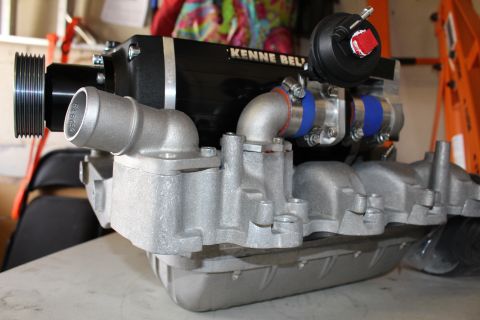 2003 Ford Crown Victoria - Side profile of a Kenne Bell supercharger showing the drive pulley, bypass valve, and blue silicone-coupled piping on a cast manifold.