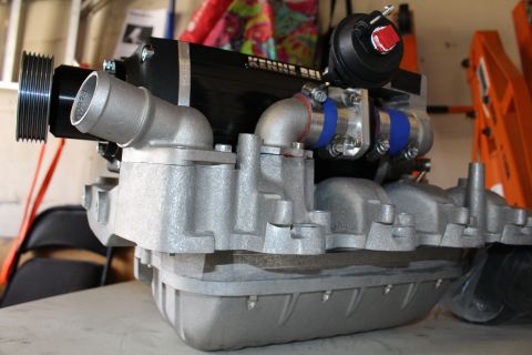 2003 Ford Crown Victoria - Low-angle view of a Kenne Bell supercharger and intake manifold assembly with pulley and bypass valve on a workbench.