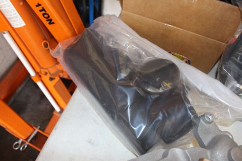 2003 Ford Crown Victoria - molded black plastic component sealed in a clear plastic bag rests on a bench beside an orange shop press.