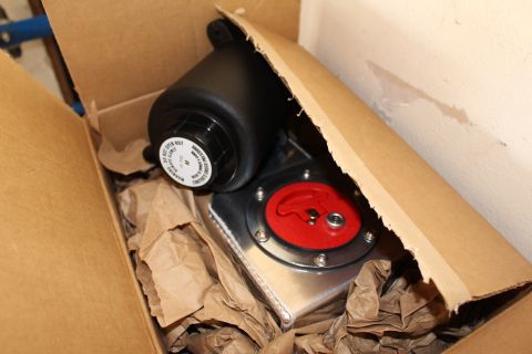 2003 Ford Crown Victoria - black canister and an aluminum plate with a red-capped fitting nestled in packing paper inside a cardboard box.
