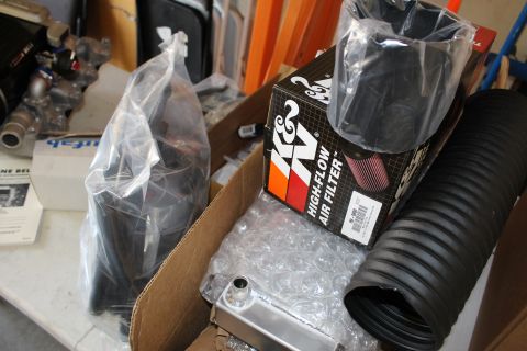 2003 Ford Crown Victoria - K&N high-flow air filter box, bagged tubing, and an aluminum intercooler core packed in a cardboard box on a garage shelf.