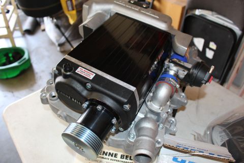 2003 Ford Crown Victoria - Angled view of a Kenne Bell supercharger with its drive pulley, throttle assembly, and warning label resting on a bench.