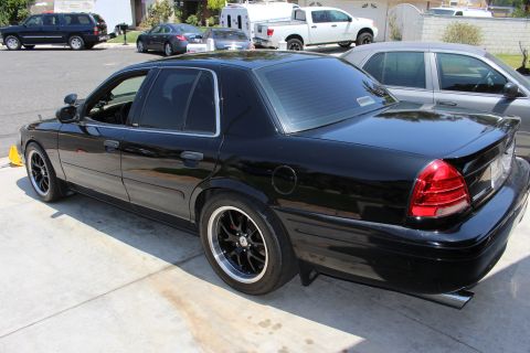 2003 Ford Crown Victoria - lowered black full-size sedan on black multi-spoke wheels poses in a driveway, shown from the rear left.