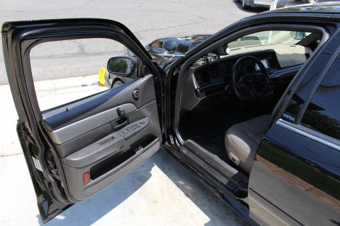 2003 Ford Crown Victoria - open driver door of a black sedan reveals a gray cloth interior; the door frame carries a VIPER decal.