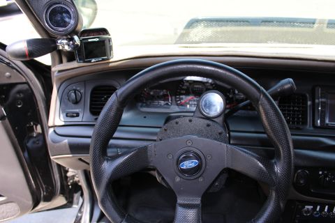 2003 Ford Crown Victoria - Close-up of a small leather Ford-badged aftermarket steering wheel ahead of the instrument cluster and A-pillar gauge.