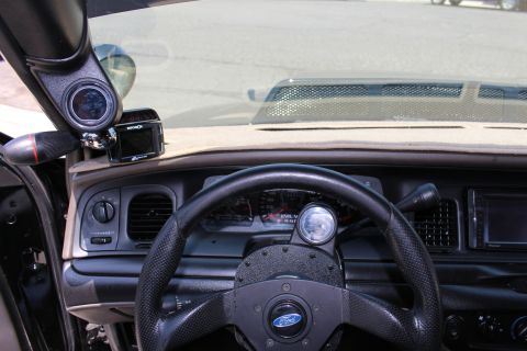 2003 Ford Crown Victoria - Dashboard of a sedan with an A-pillar boost gauge, windshield-mounted detector, aftermarket wheel and stereo head unit.