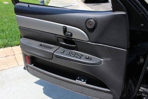 2003 Ford Crown Victoria - driver door panel of a sedan, showing the armrest pull, power-window and lock switches, viewed with the door open.