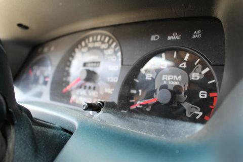 2003 Ford Crown Victoria - Close-up of a dusty instrument cluster showing the speedometer, tachometer, and warning lights of a vehicle.