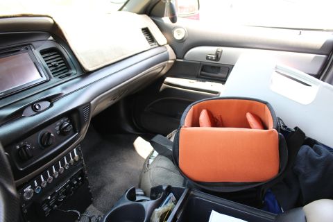 2003 Ford Crown Victoria - View across the front interior showing the dash, switch panel, and an open orange-lined camera bag on the passenger seat.