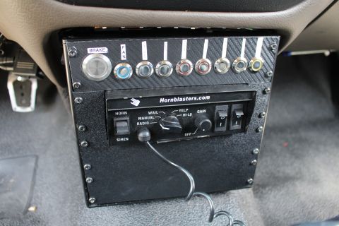2003 Ford Crown Victoria - Custom carbon-fiber under-dash panel with a HornBlasters siren controller, a brake button, and a row of labeled toggle switches.