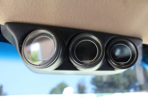 2003 Ford Crown Victoria - Trio of round auxiliary gauges housed in a black pod mounted beneath a tan headliner, photographed against a blue sky.