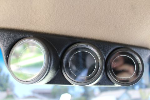 2003 Ford Crown Victoria - Close-up of three round auxiliary gauges in a black housing mounted under tan interior trim with outdoor greenery reflected.