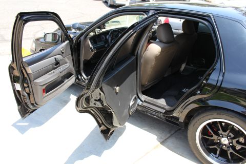 2003 Ford Crown Victoria - Black four-door sedan parked with its front and rear doors open, revealing tan seat covers and dark alloy wheels.
