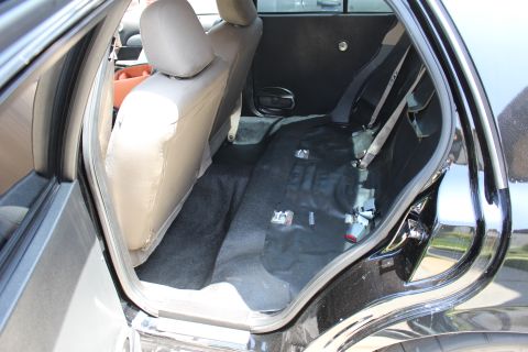 2003 Ford Crown Victoria - Sedan rear interior with the lower bench cushion removed, exposing the carpeted floor pan and seat belt hardware.