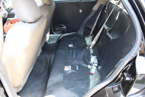 2003 Ford Crown Victoria - Back seat of a sedan with the bottom cushion lifted out, revealing the carpeted floor, seat belts, and buckle hardware.