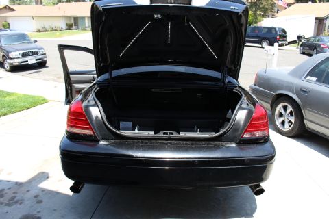 2003 Ford Crown Victoria - Rear of a black sedan with its trunk open in a residential driveway, showing dual exhaust tips and LED strips inside the trunk lid.