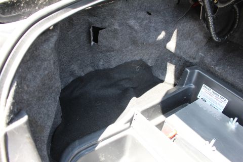 2003 Ford Crown Victoria - Empty carpeted trunk well next to a Police Trunk Pack metal equipment tray with a torn carpet section visible.