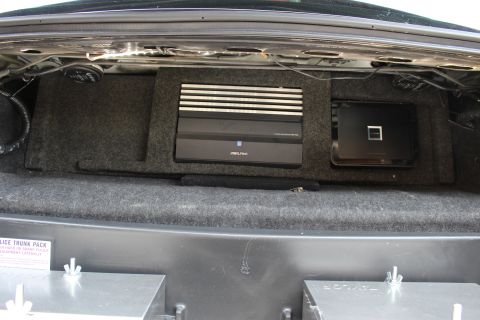 2003 Ford Crown Victoria - Alpine amplifier and a black electronics unit mounted to the carpeted rear deck inside an open car trunk.