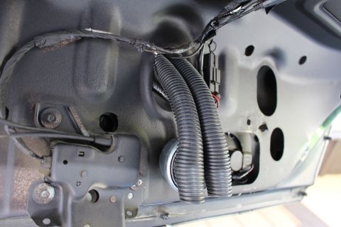 2003 Ford Crown Victoria - Black corrugated wiring conduit and a harness routed across gray painted automotive sheet metal near a latch.