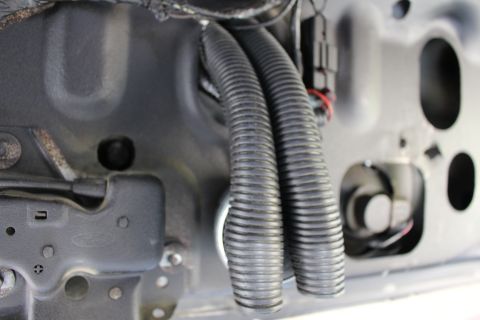 2003 Ford Crown Victoria - Two black corrugated wiring conduits loop across a gray painted body panel beside a grommet hole.