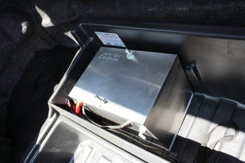 2003 Ford Crown Victoria - bare-metal Taylor box with a red battery clamp and wiring secured in a black trunk tray with a label tag.