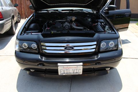 2003 Ford Crown Victoria - black Ford sedan with the hood raised showing the engine, chrome grille and a California EVIL VIC license plate.