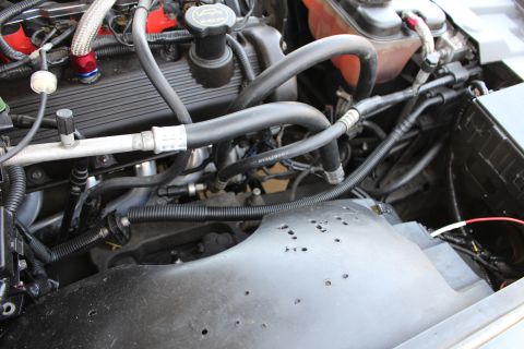 2003 Ford Crown Victoria - close-up of an engine valve cover with rubber vacuum hoses, braided lines and the painted inner fender behind.