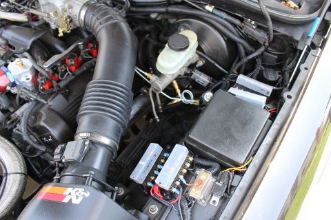 2003 Ford Crown Victoria - close view of a black K&N intake tube, brake master cylinder reservoir, fuse box and relays in an engine bay.