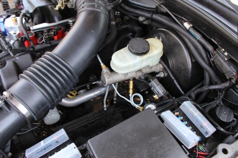 2003 Ford Crown Victoria - Close-up of a translucent brake master cylinder reservoir beside a corrugated black air intake tube and battery in the engine bay.