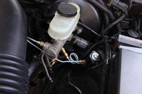 2003 Ford Crown Victoria - Detail shot of a brake master cylinder reservoir mounted on a metal valve body with brass line fittings and wiring.