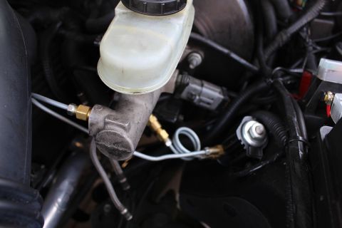 2003 Ford Crown Victoria - Tight close-up of a weathered brake master cylinder and proportioning valve with brass brake-line fittings and a return spring.