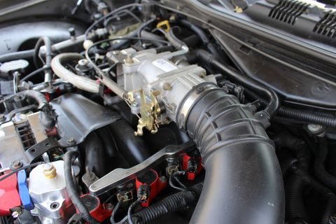 2003 Ford Crown Victoria - Close-up of an aluminum throttle body and large black intake elbow with red ignition coil packs and braided wiring below.