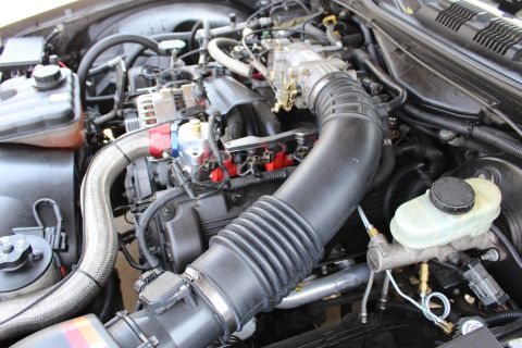 2003 Ford Crown Victoria - Engine bay view with a chrome-trimmed alternator, large black intake elbow, throttle body and brake master cylinder reservoir.