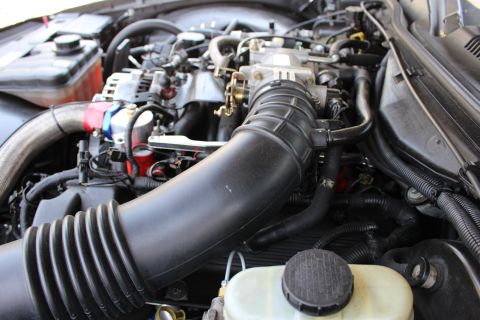 2003 Ford Crown Victoria - Engine bay dominated by a large black corrugated air intake tube curving to the throttle body above the brake reservoir.