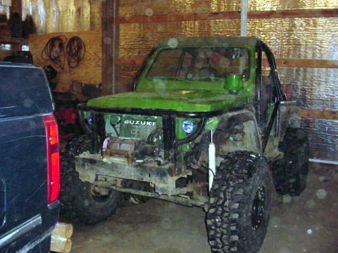 1992 Ford Bronco - A modified green Suzuki Samurai is parked indoors next to a black vehicle.