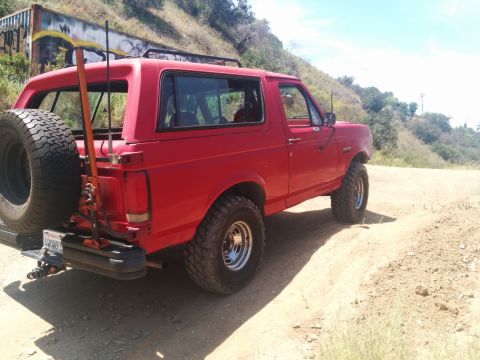 1988 Ford Bronco - This red 1988 Ford Bronco is seen from the rear, parked on a dirt road with a spare tire mounted on the back.