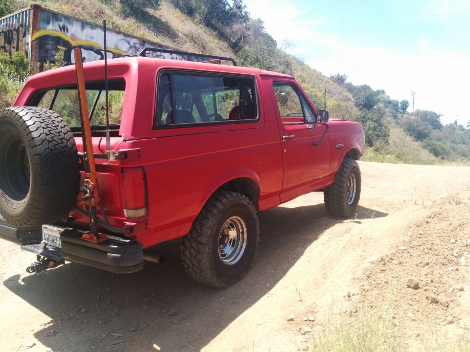 Red 1988 Ford Bronco with spare tire mounted on rear swing away carrier