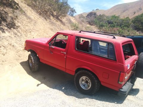 1988 Ford Bronco - This red Ford Bronco is parked on a dirt road with hills in the background.