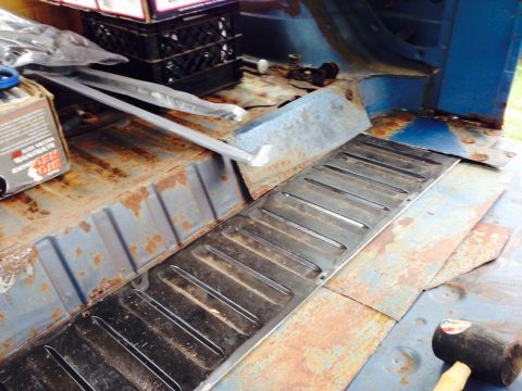 1979 Ford Bronco - The interior of a vehicle shows significant rust and a newly installed metal floor panel, with boxes and other items in the background.