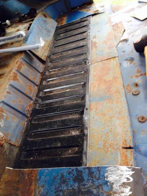 1979 Ford Bronco - The interior floor of a vehicle shows significant rust and a black ribbed vent panel.