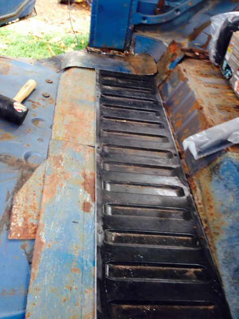 1979 Ford Bronco - The interior of a blue vehicle shows extensive rust damage on the floor panels, with a new metal section being fitted.