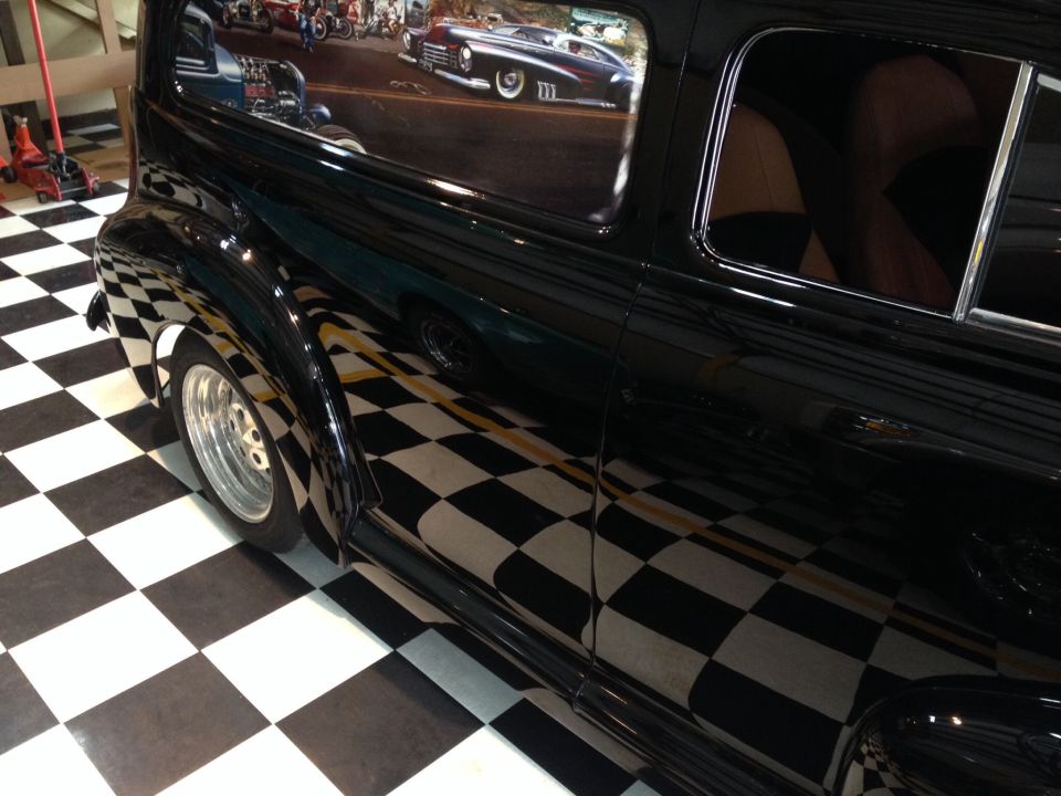 Black car side view, chrome trim, custom wheels, reflection of checkerboard floor and mural
