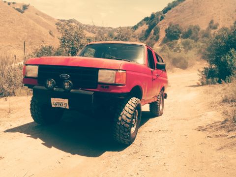 1988 Ford Bronco - This red Ford Bronco is equipped for off-road use and is seen on a dusty trail.