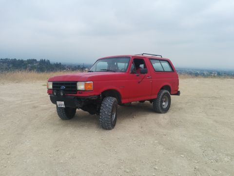 1988 Ford Bronco - This red 1988 Ford Bronco is shown from a three-quarter front view, parked outdoors on a dusty incline.