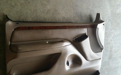 1994 Ford Bronco - A tan car door panel with wood trim and a torn speaker grille is shown.