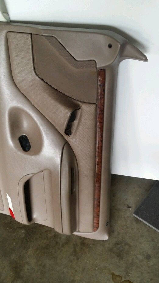 Tan plastic door panel with wood trim and a torn section near the handle