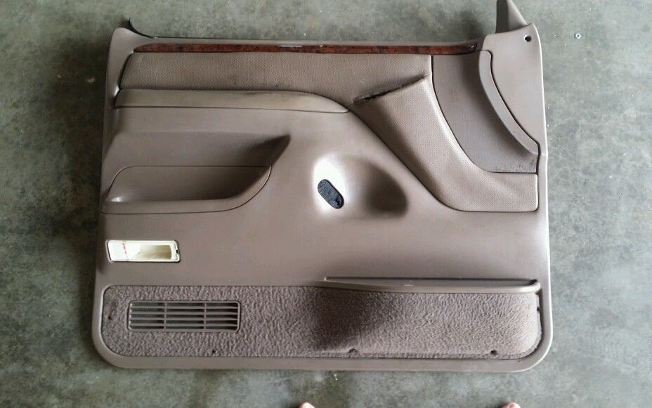Tan car door panel with wood trim, speaker grille, and storage pocket
