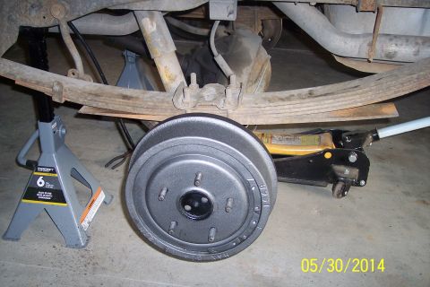 1978 Ford Bronco - The rear suspension and brake drum of a vehicle are visible, supported by jack stands and a hydraulic jack.